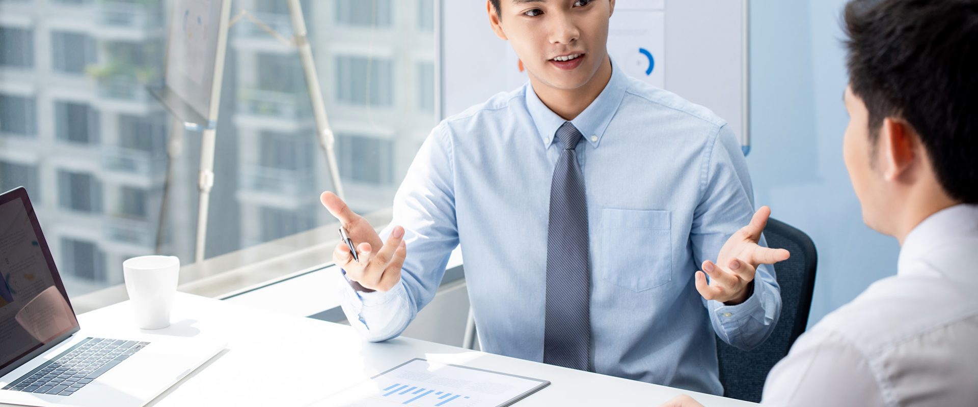 Attractive Asian financial broker explaning business data to his client during their private meeting in the office